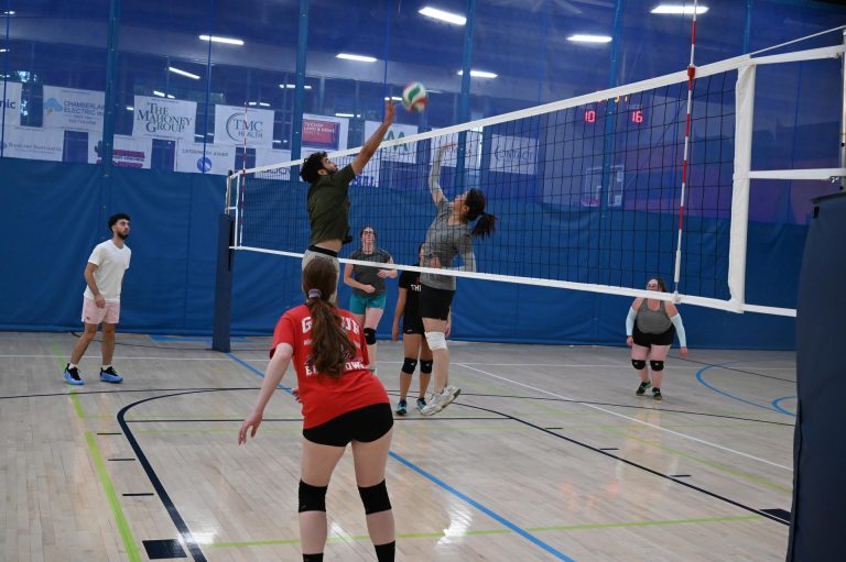 Adults slam a volleyball across the net