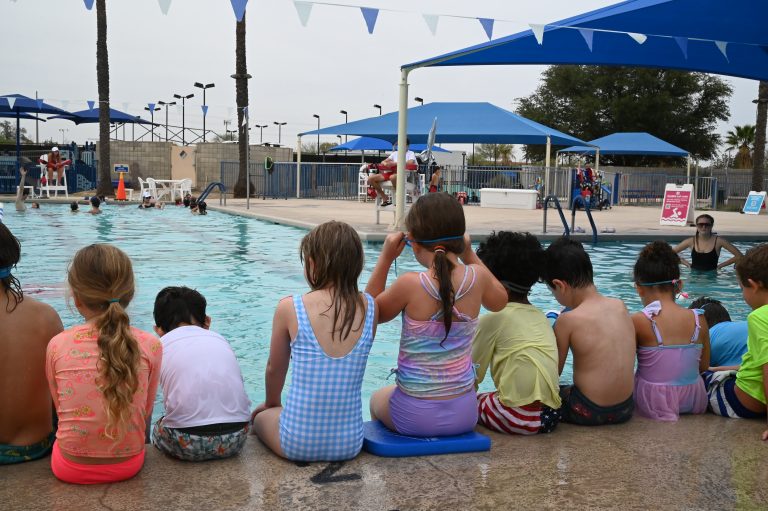 Kids sitting along a pool in bathing suits