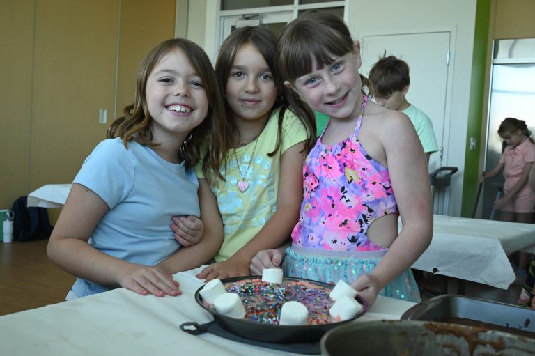 three girls smiling around a cake