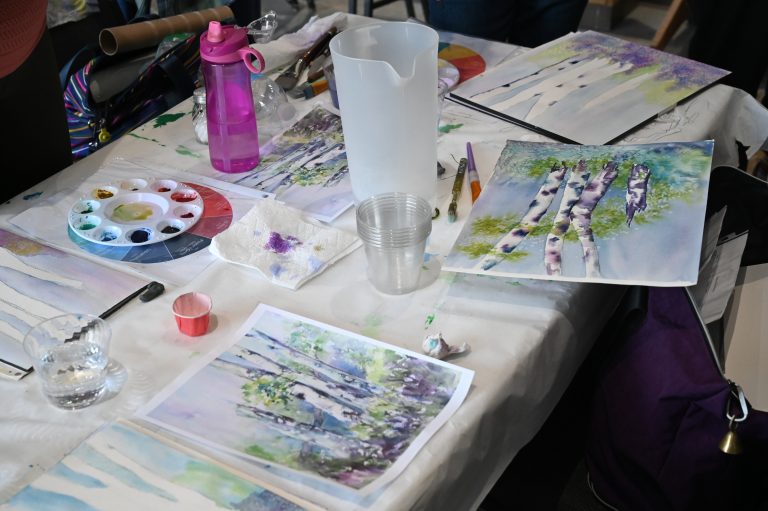 art class table with watercolor supplies and paintings