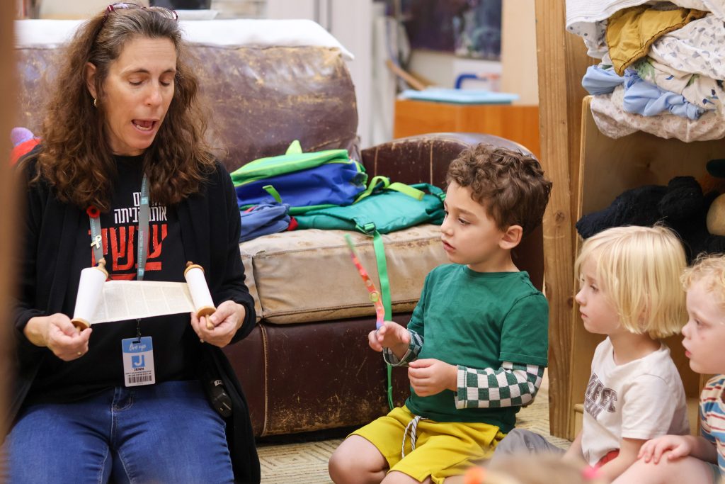 An adult woman holds the Torah while sitting on the floor next to two children