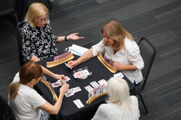 Four adult women sit around a table playing a card game.
