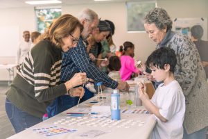 Three elderly adults and one child paint ceramic flowers