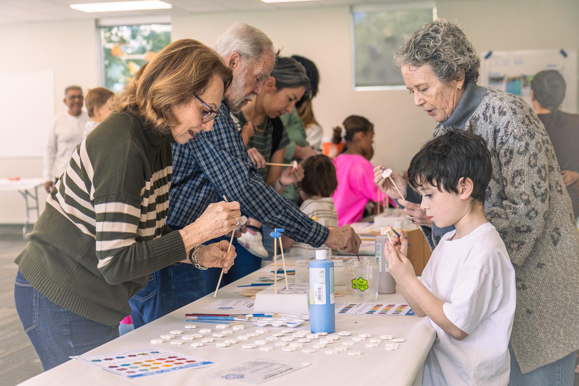 Three elderly adults and one child paint ceramic flowers