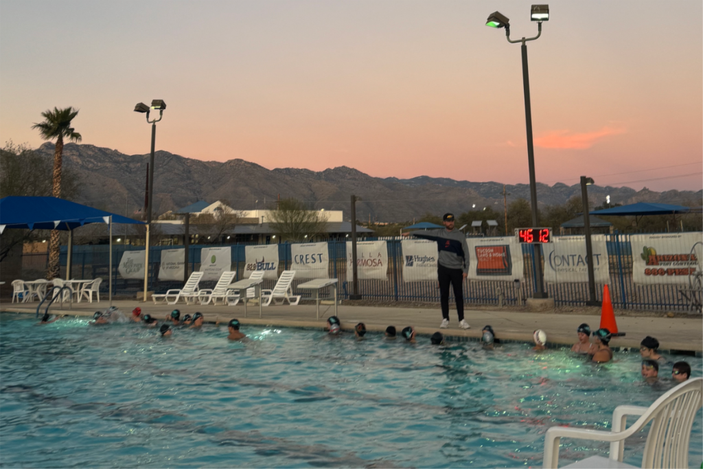 Kids swim in a large pool with a sunset and mountains in the background