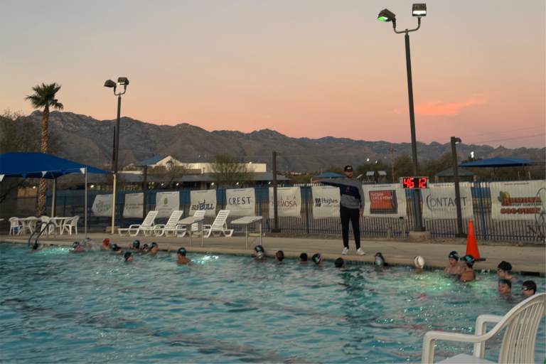 Kids swim in a large pool with a sunset and mountains in the background