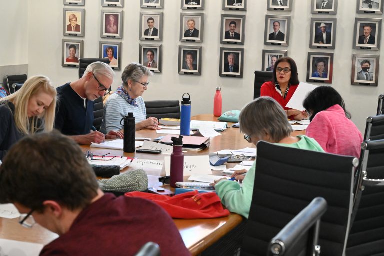 Adults sit around a table with paper and binders