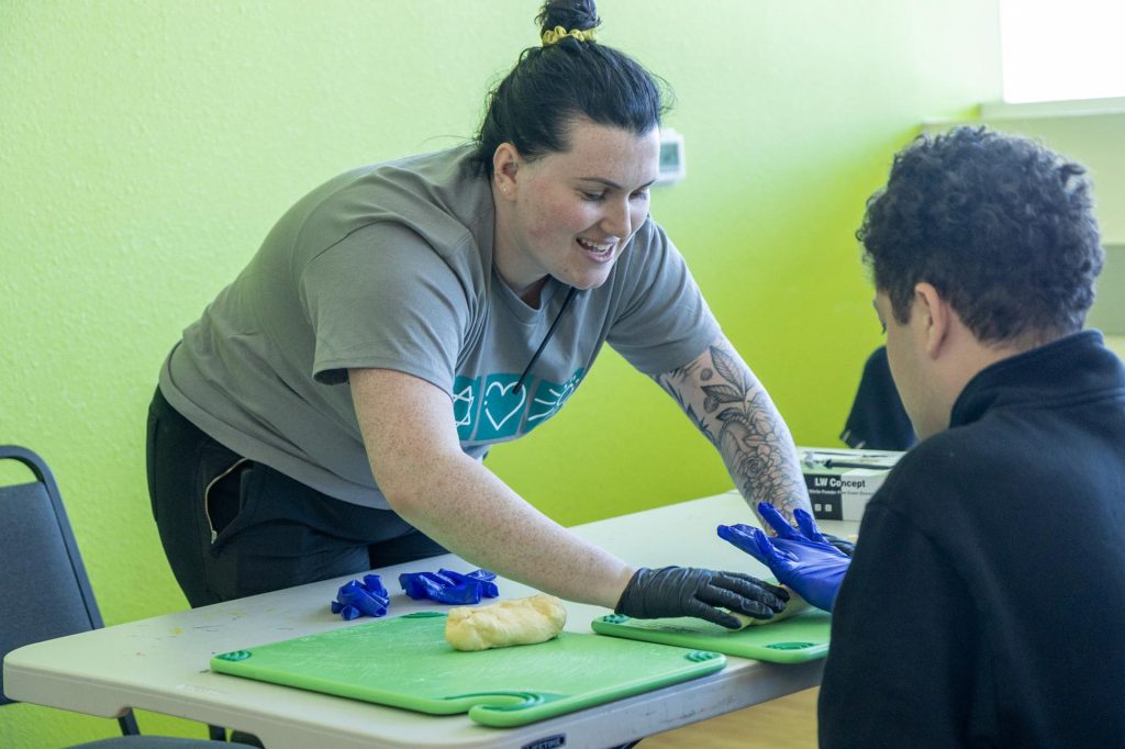 An adult woman rolls out dough, assisting another adult