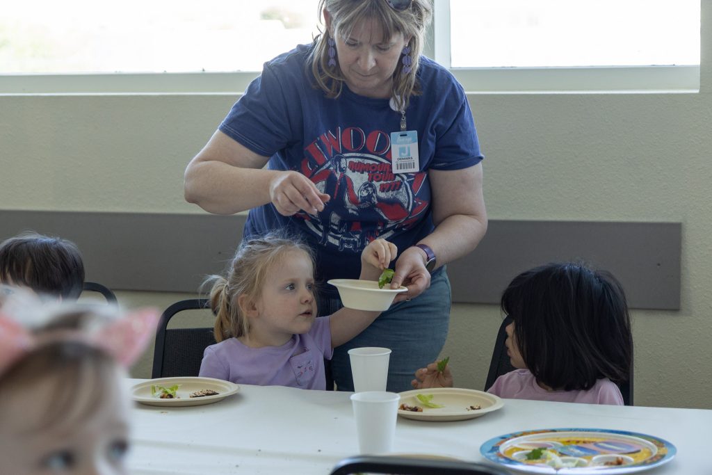 An adult hands a child, sitting at a table, a paper bowl