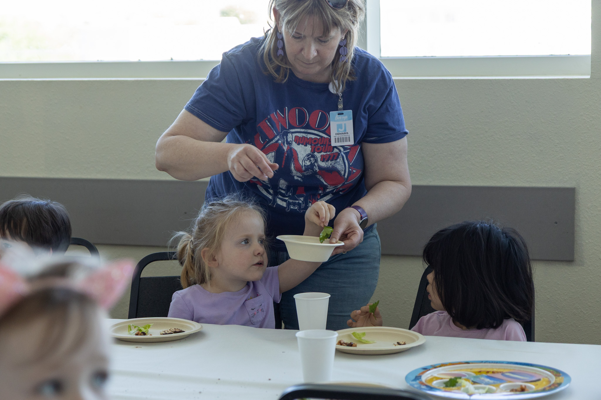 An adult hands a child, sitting at a table, a paper bowl