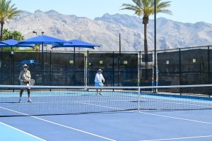 Adults play tennis outside on a court